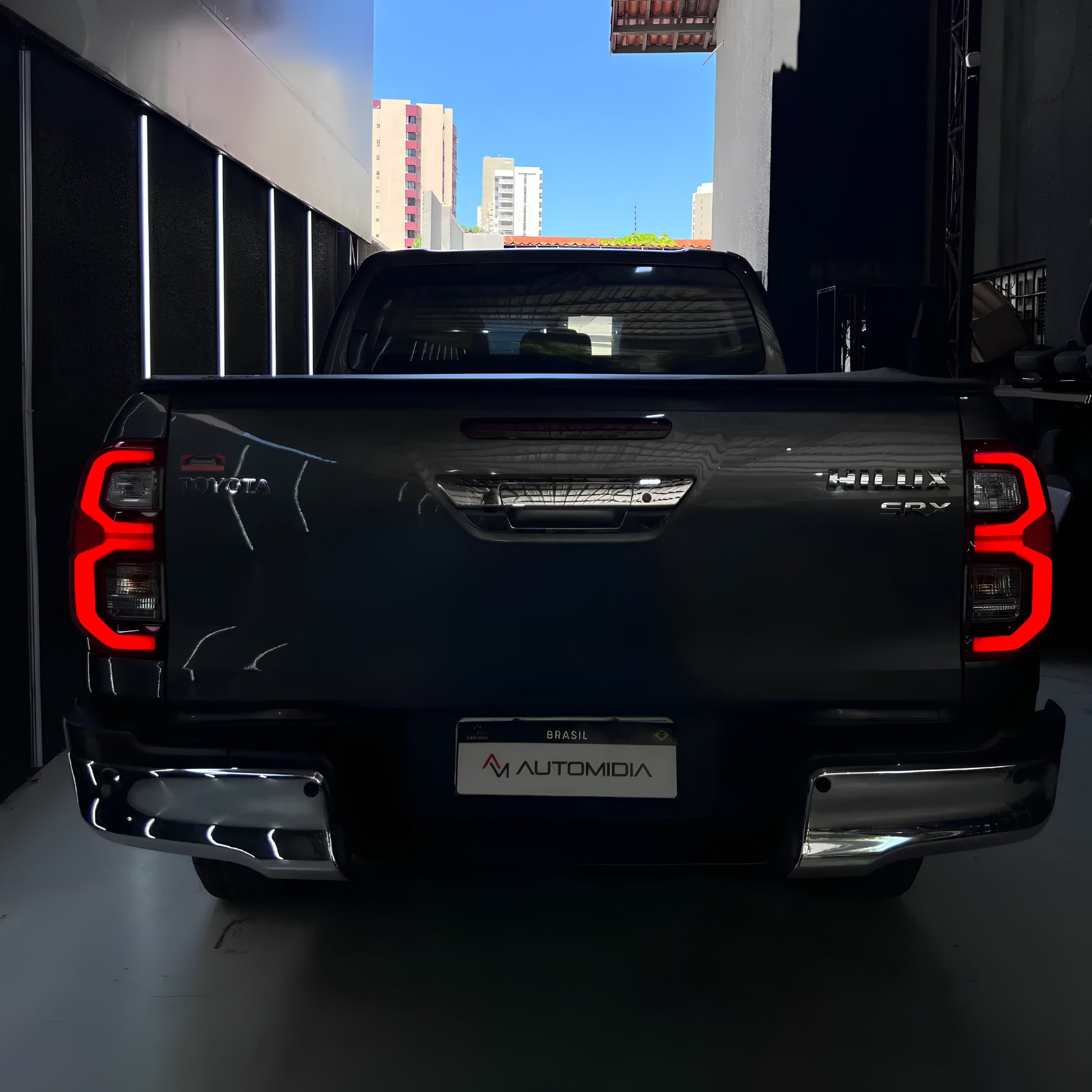 Toyota Hilux SRX 2026 transformada em vista traseira, com lanternas LED acesas, tampa da caçamba, para-choque cromado e acabamento atualizado.